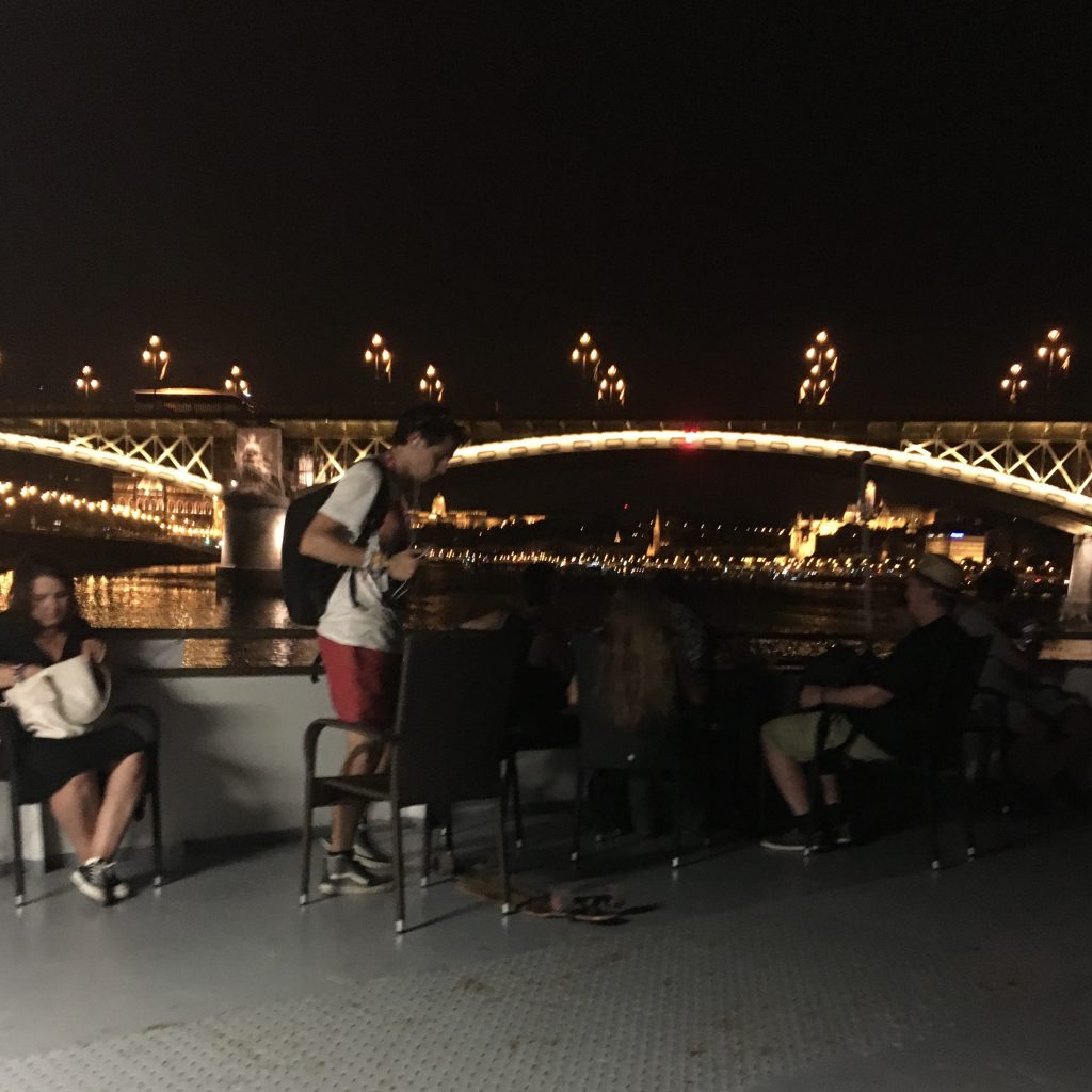One of the many lit up Budapest bridges can be seen from a boat at night time.