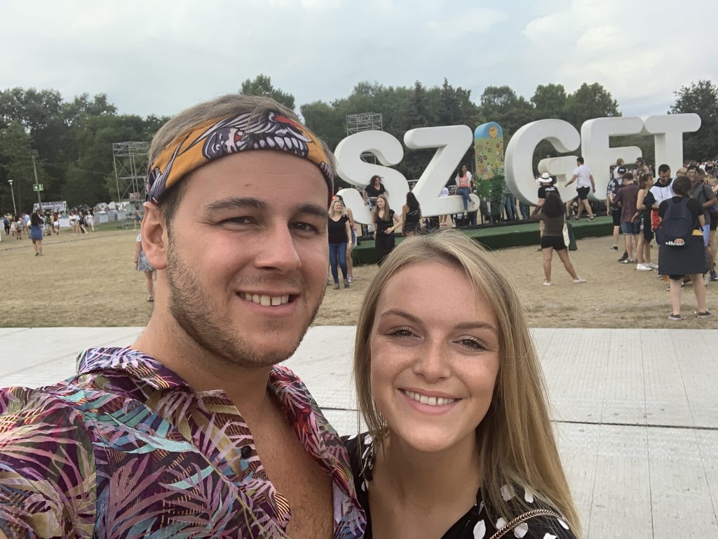 Two people stood taking a selfie in front of the Sziget decoration sign.