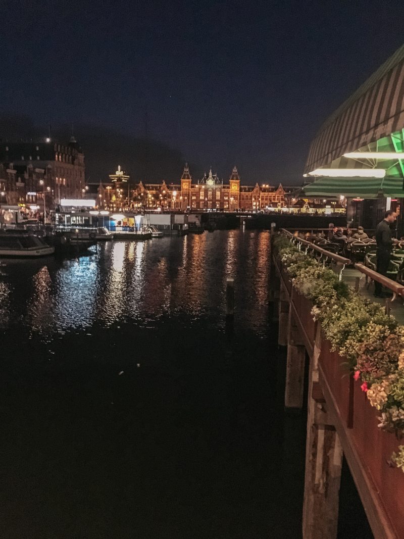 A view of the Amsterdam train station at night across the water. Amsterdam on a budget