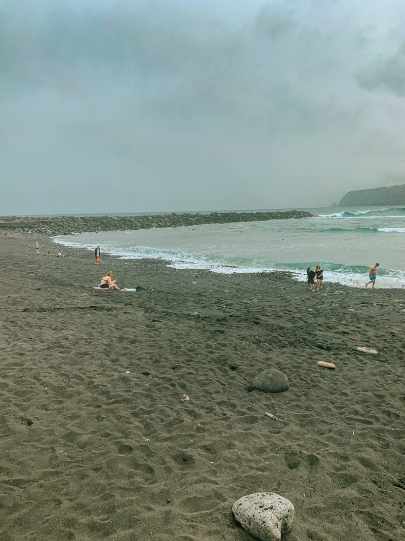 Black sandy beach with some people on it. Where to stay in Tenerife