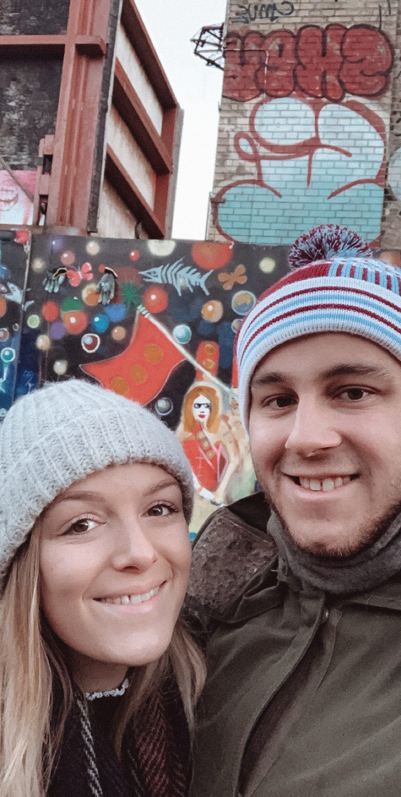 Two people having a selfie in front of graffiti.