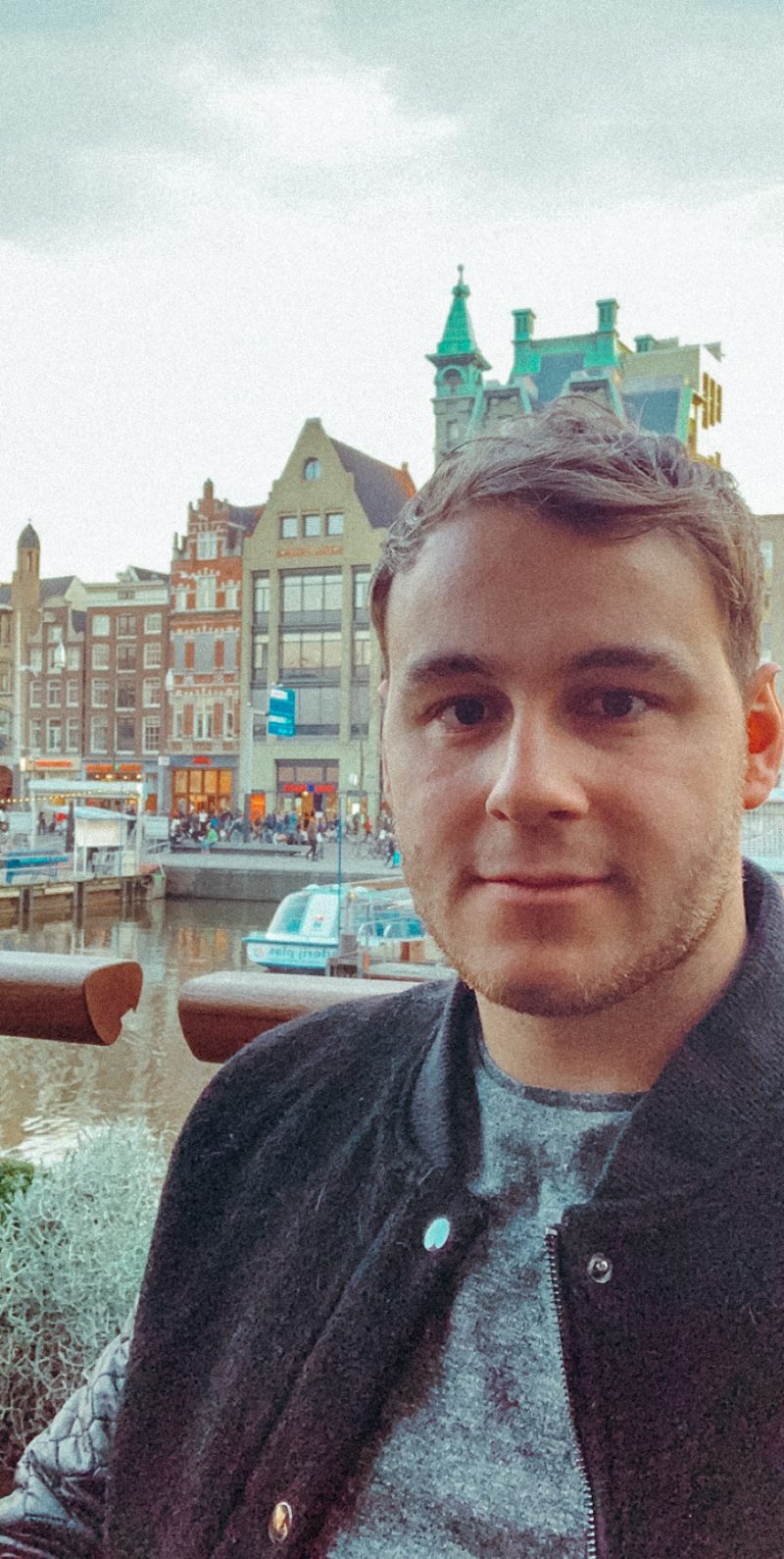 A man posing infront of buildings in Amsterdam