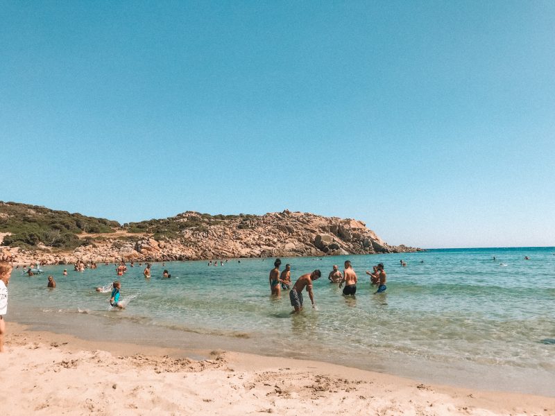 People splashing in the turquoise ocean and on the sand. What to do in Sardinia
