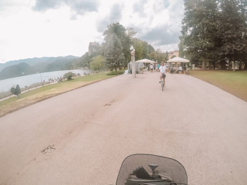 A woman in front of the camera riding a bike around Lake Bled. What to do at Lake Bled
