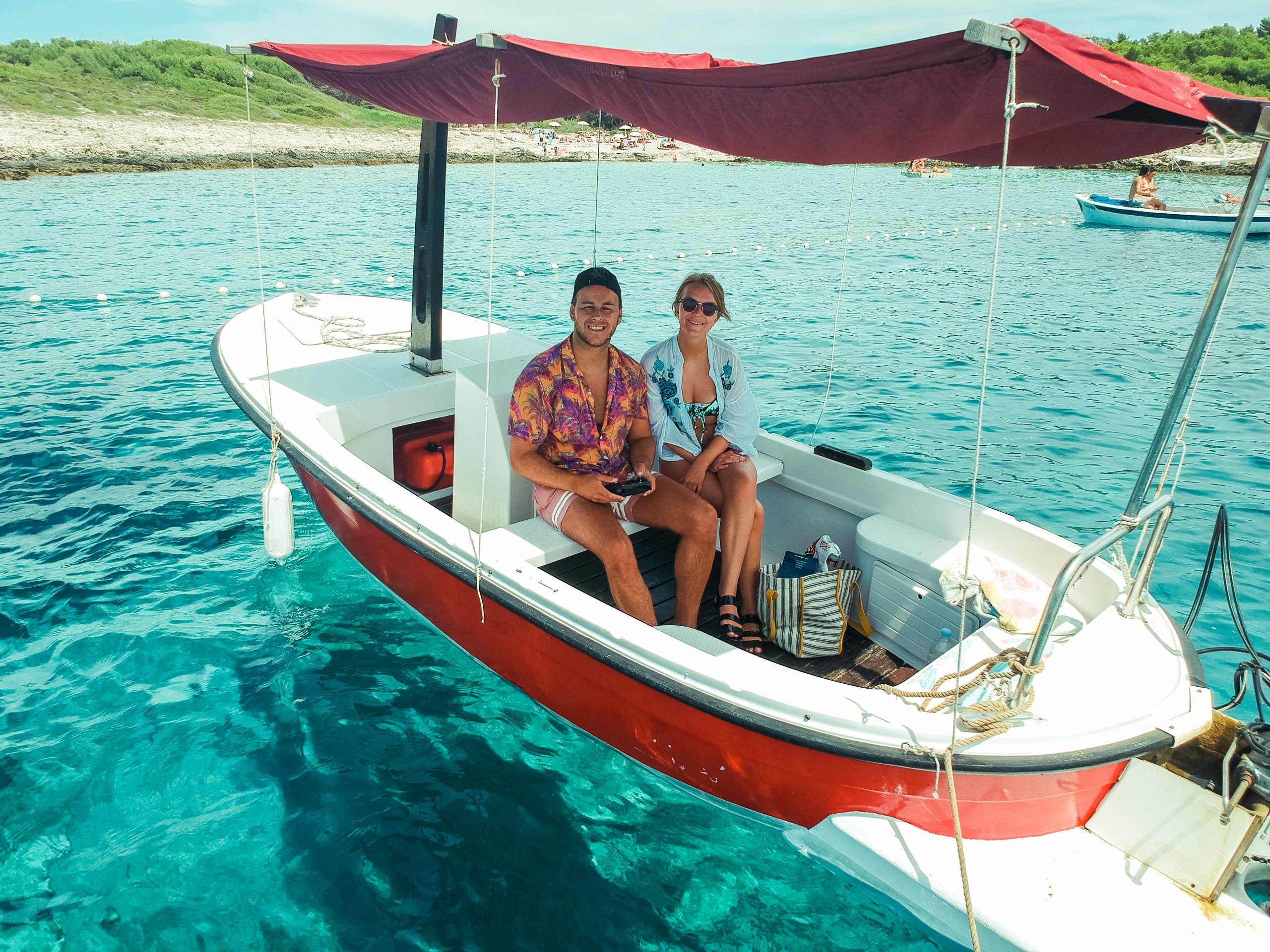 A couple sat in a rented boat, surrounded by turquoise water. Things to do in Hvar