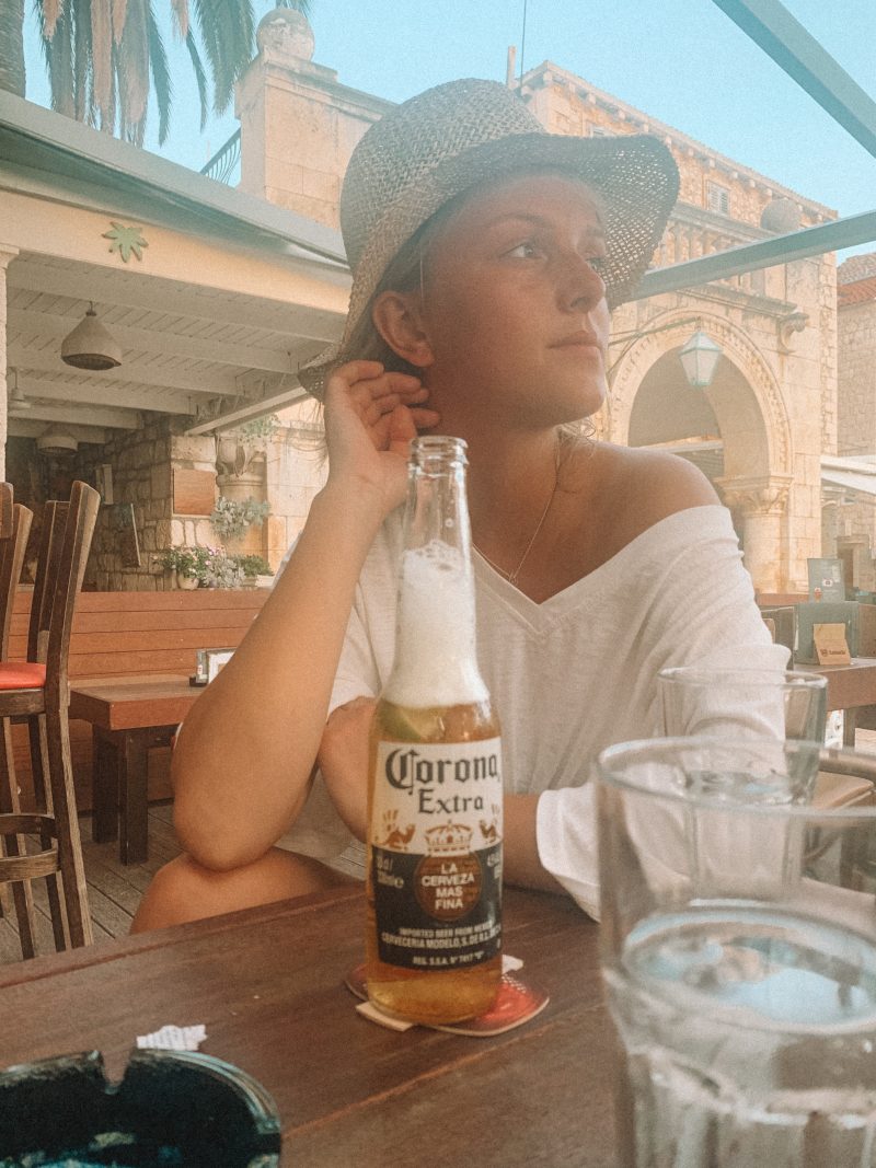 A woman in a straw hat sat drinking a bottle of Corona at a table. What to do in Hvar