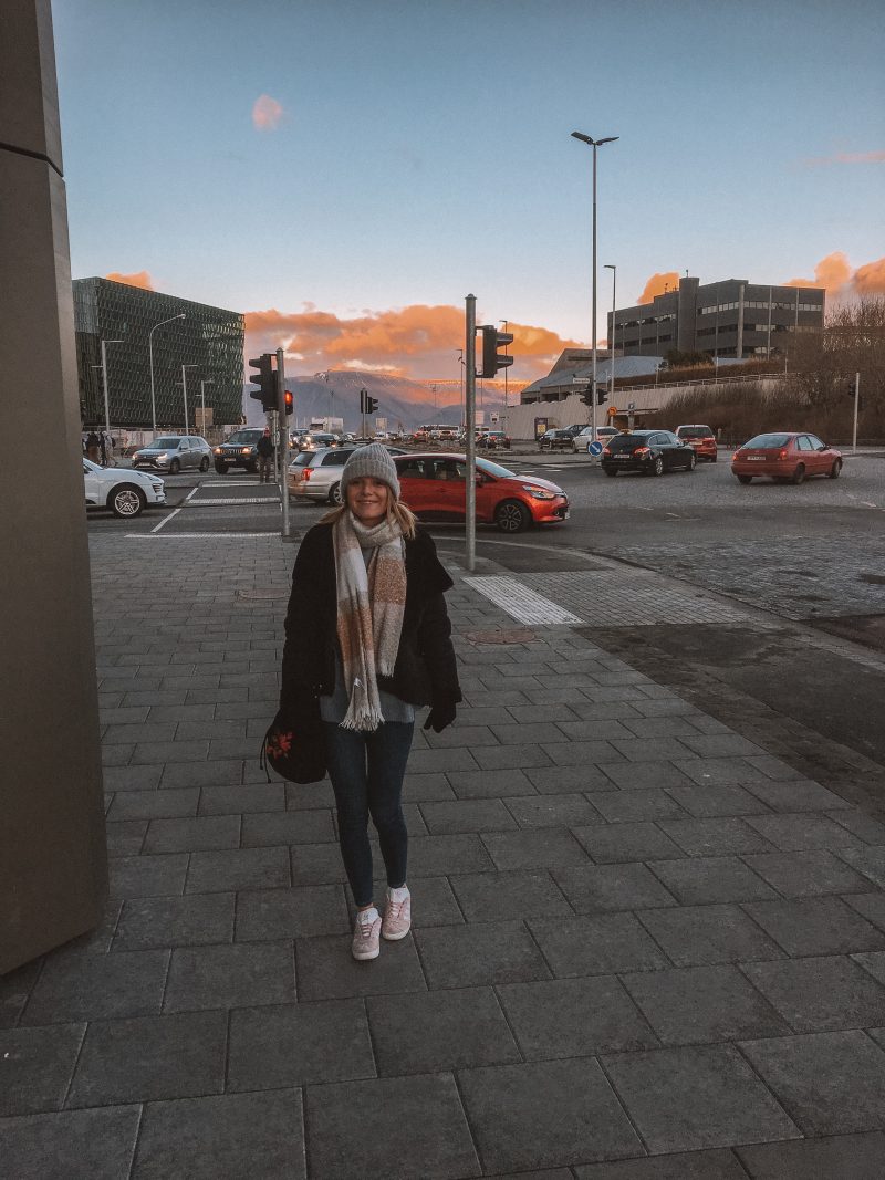 A woman in Reykjavik with the Harpa Concert Hall in the background as part of the things to do in Reykjavik, Iceland.