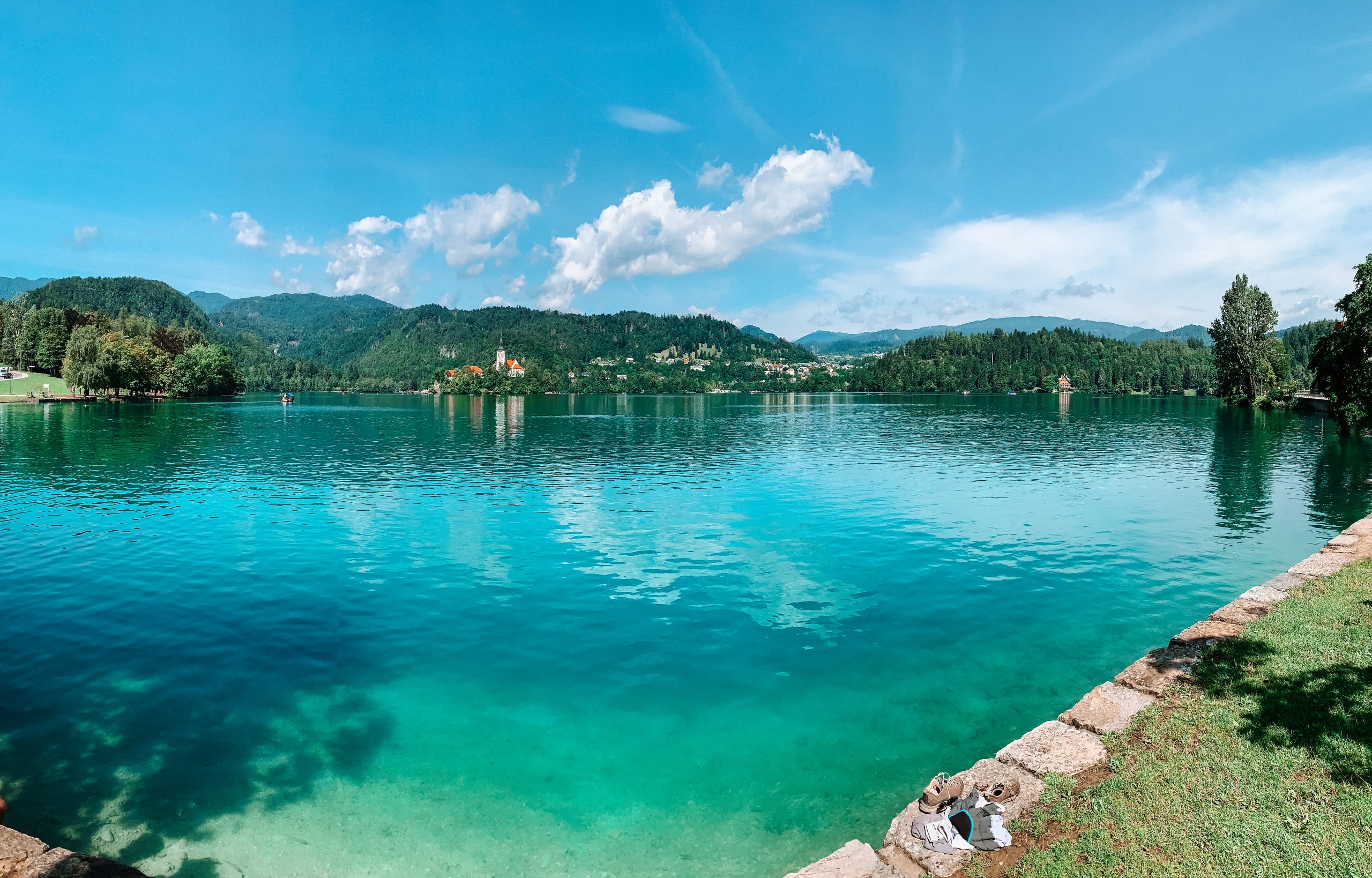 A wide angle view of Lake Bled and its surrounding areas with hills and an island in the background