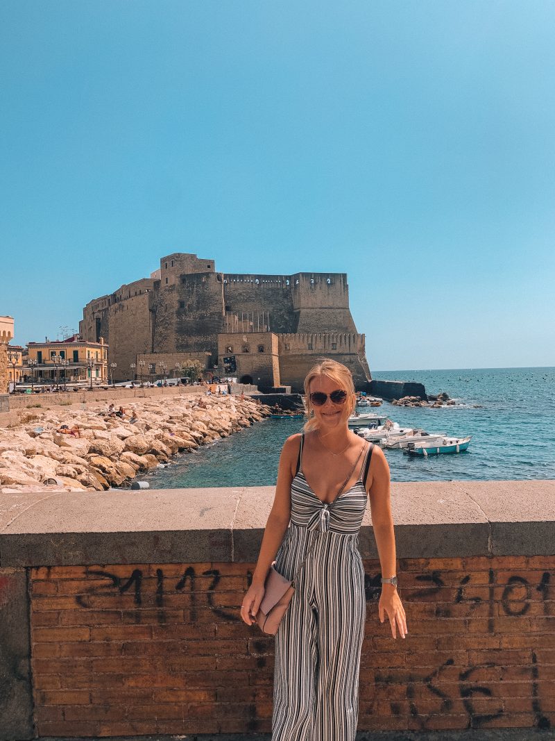 A woman posing next to graffiti and Naples castle. Where to go in Naples