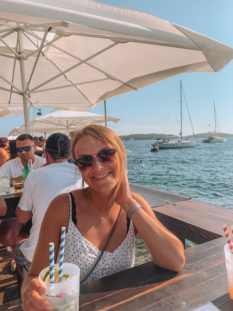 A woman having a cocktail in Hula Hula bar with the ocean in the background. Things to do in Hvar