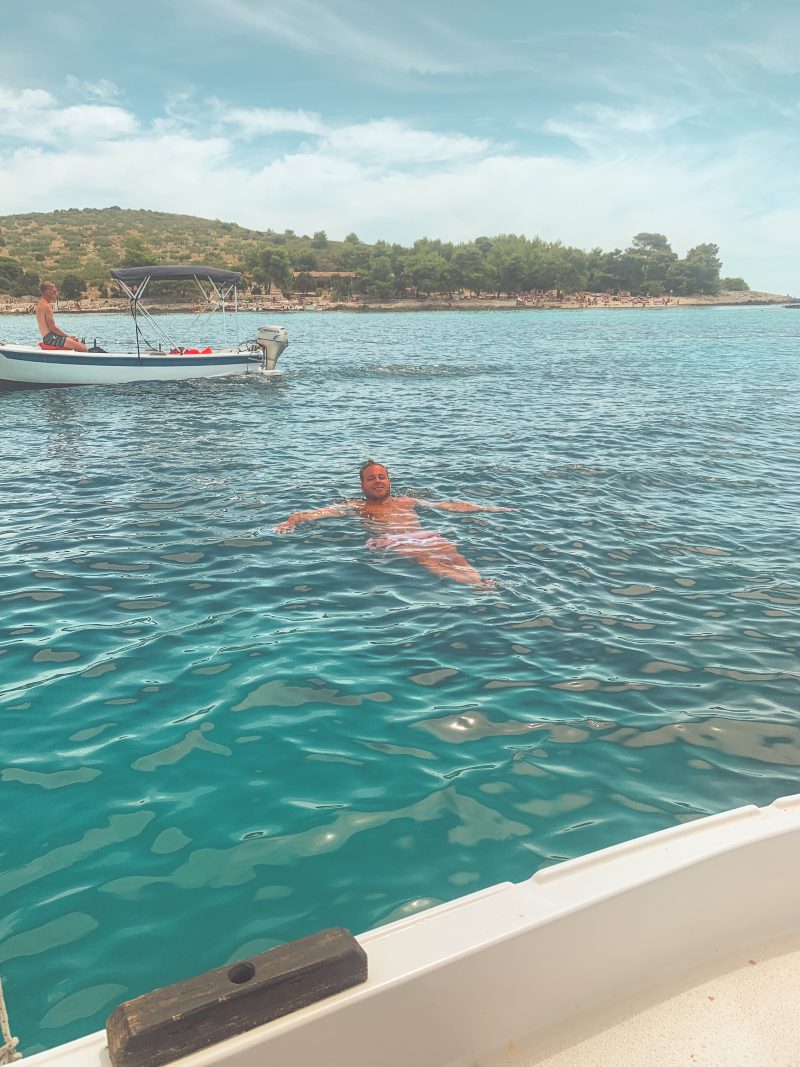 A man swimming in turquoise water near a boat. Things to do in Hvar