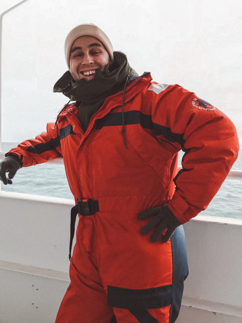 A man dressed with thick layers with the ocean behind as part of whale watching in Iceland