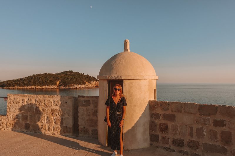 A woman stood in front of a turret on the Dubrovnik city walls with Lokrum in the distance