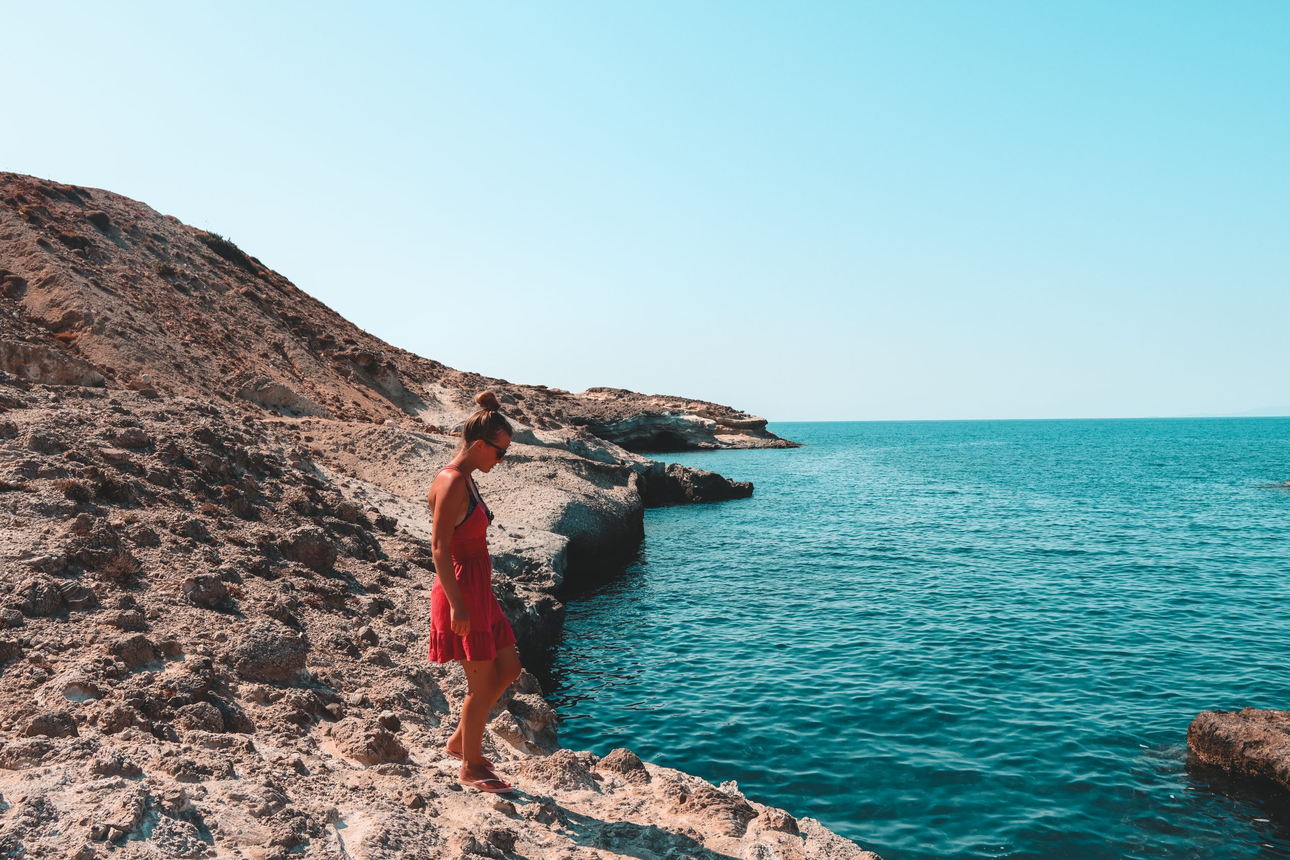 A woman stood next to the turquoise sea at Kapros beach in Milos