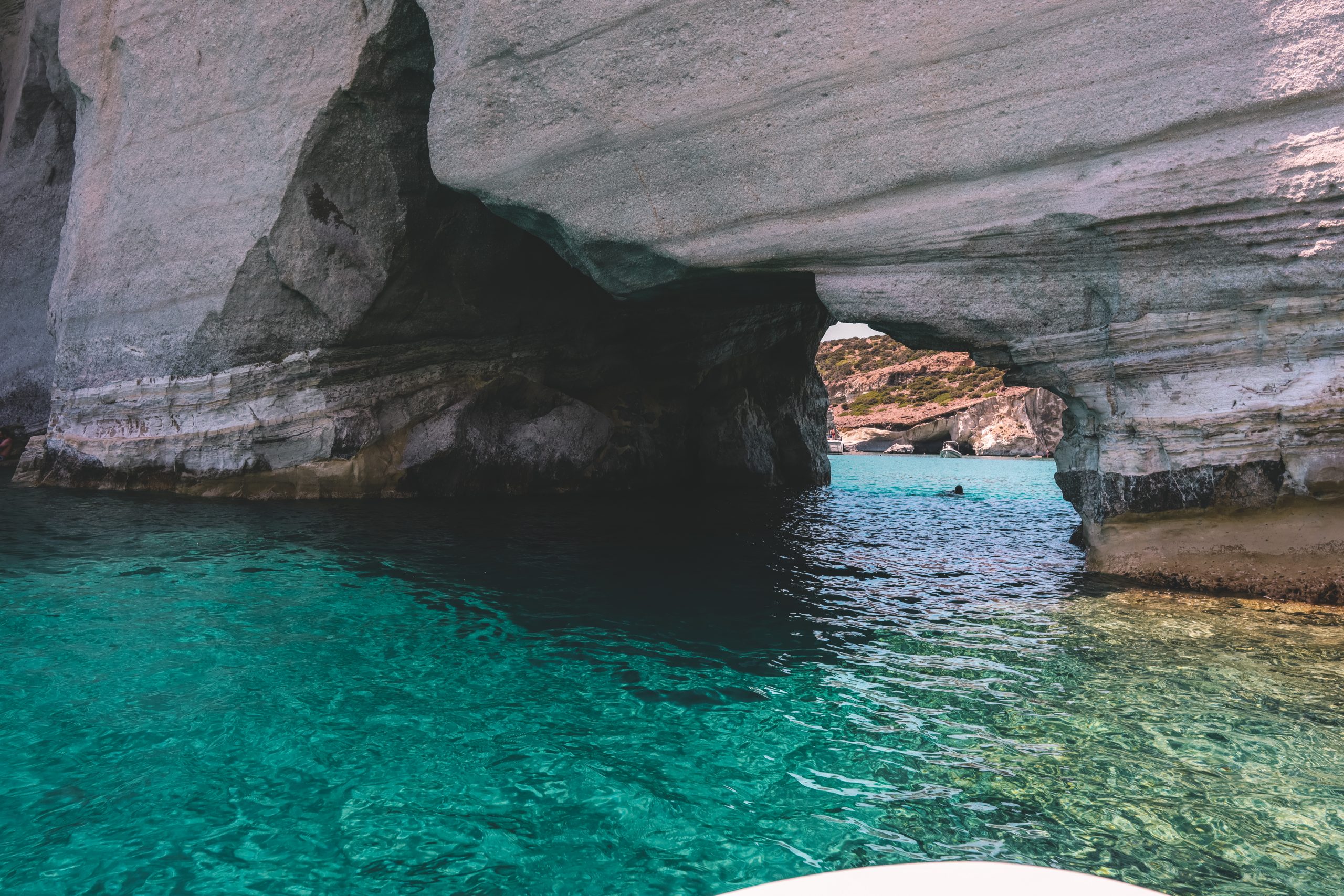 A person swimming in clear water through a cave. Things to see in Milos