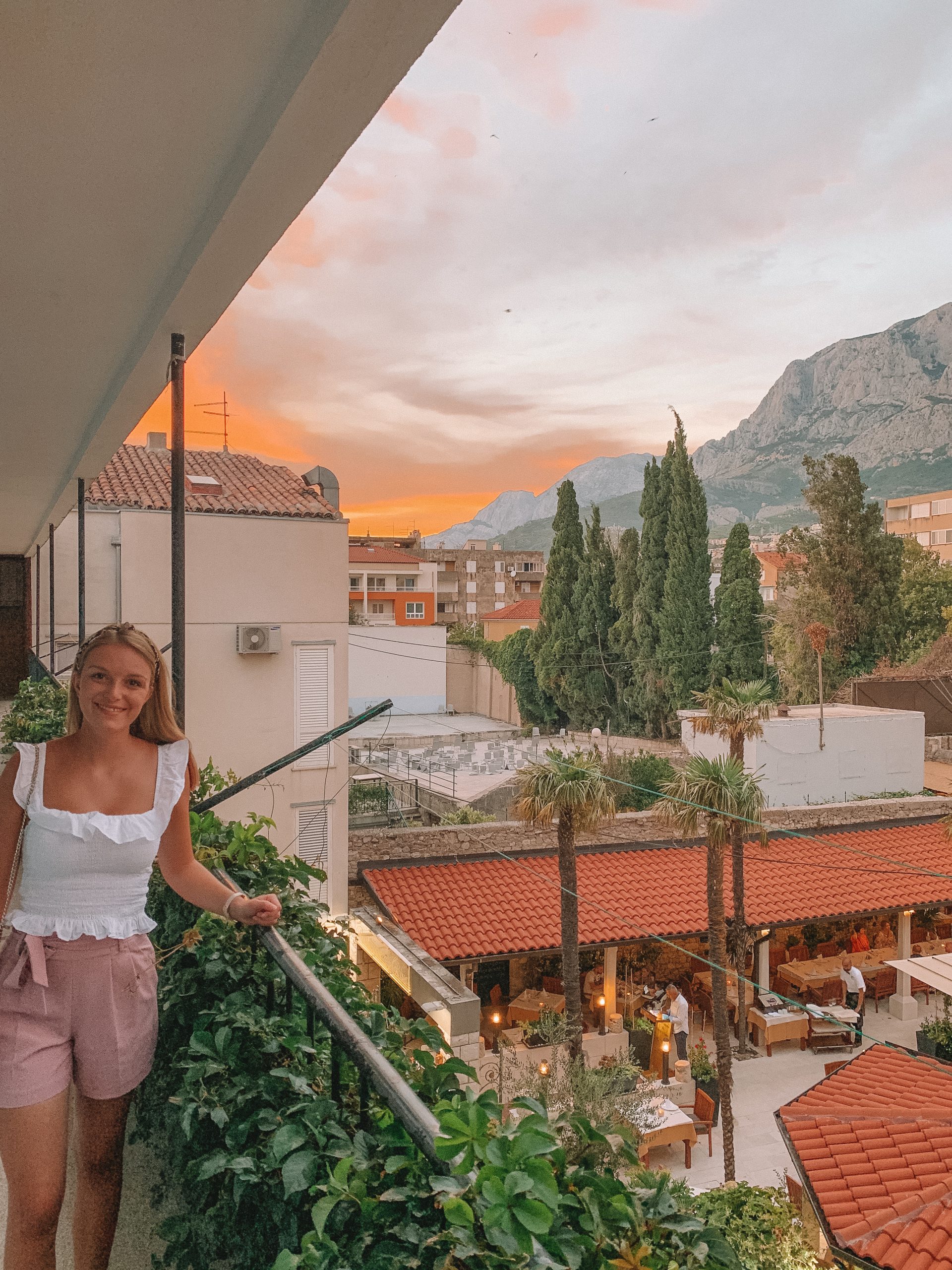 A woman stood on her balcony with the sunsetting over the mountains