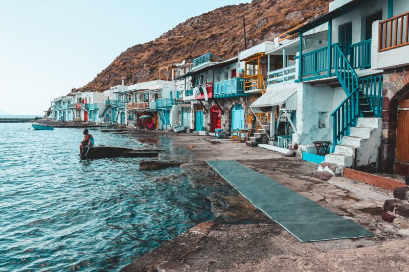 Colourful fishing area at Kilima in Milos. A man sits looking to the ocean. Things to do in Milos.