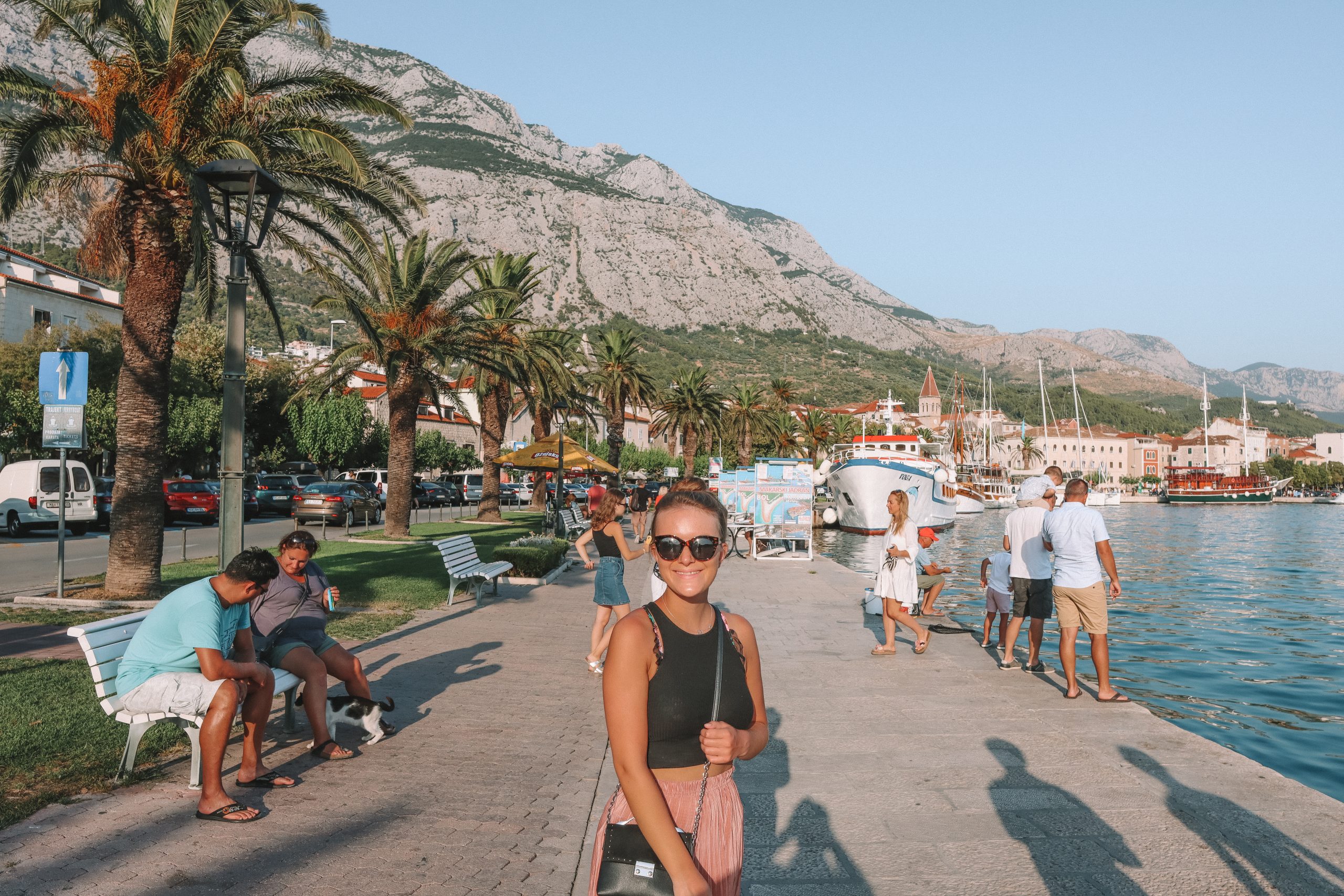 A woman stood on the promenade with palm trees and mountain in the background. Your guide to Makarska.