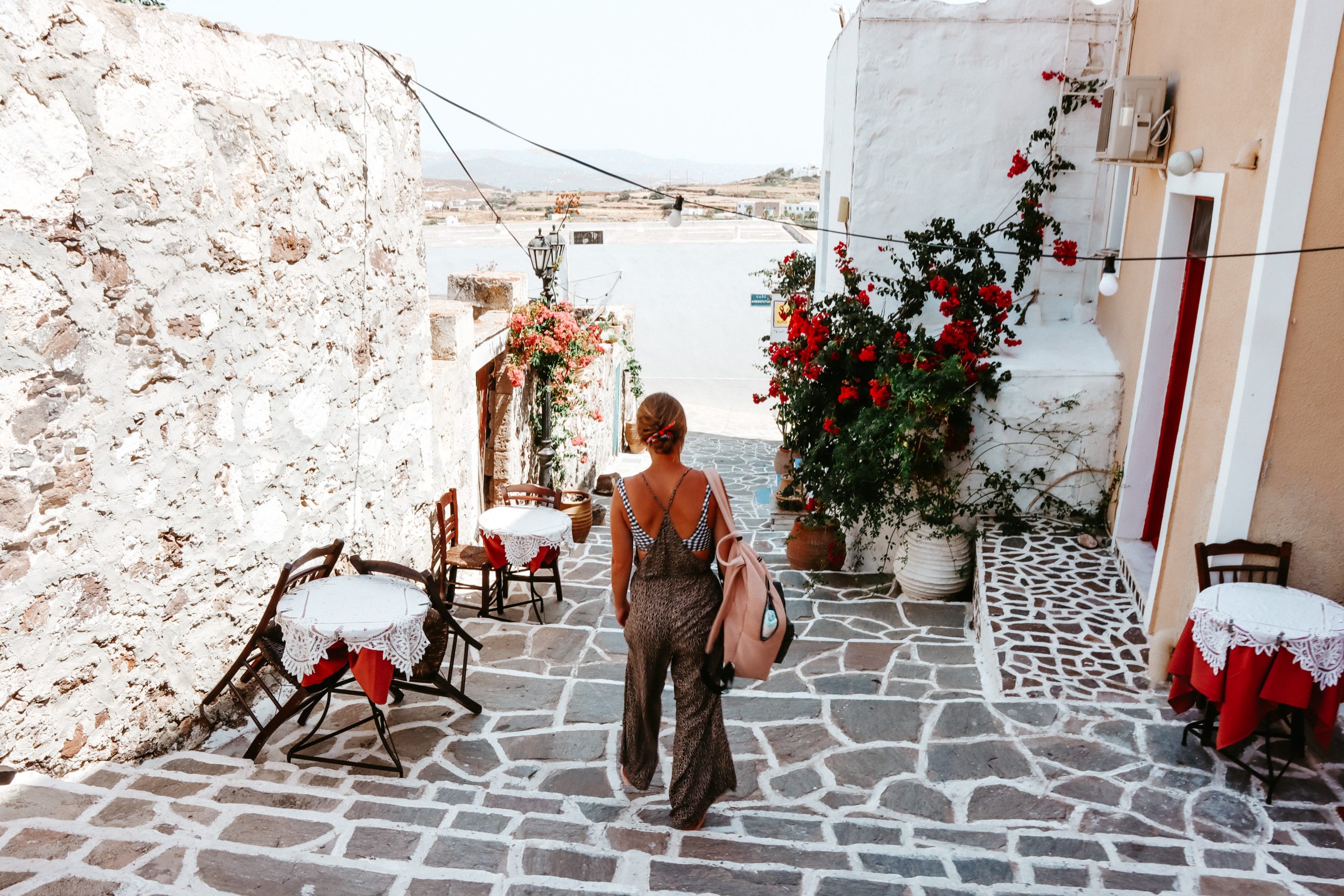 A woman walking down a narrow Greek street with flowers decorated around. Things to do in Milos