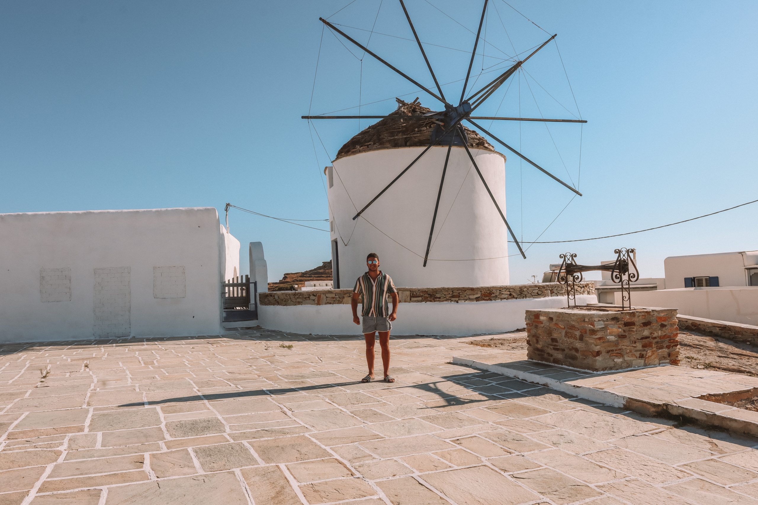A man carrying invisible carpets in front of a windmill in Ios
