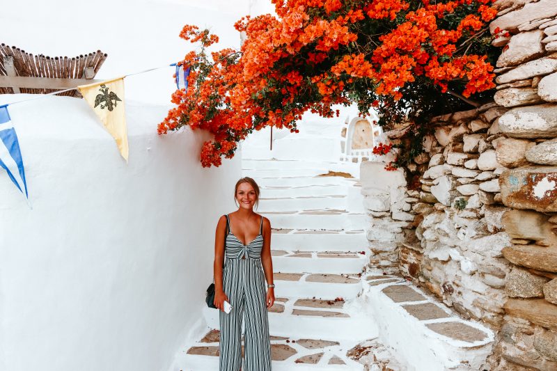 A woman stood in the Chora streets in Ios with flowers in the background. Things to do in Ios
