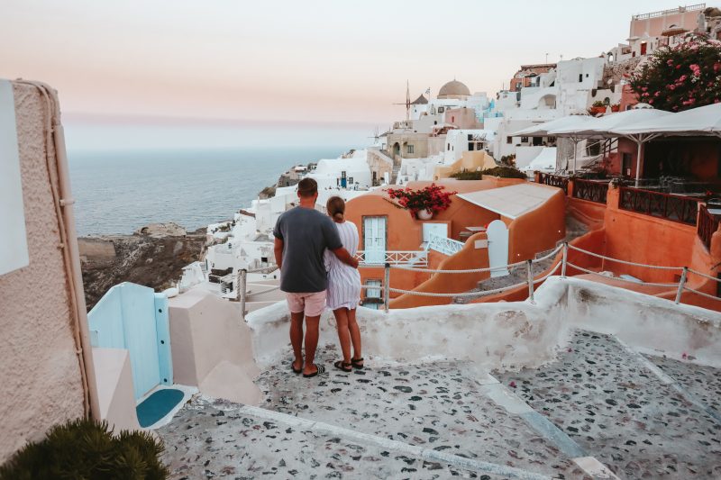 A couple looking out to sea with the pastel buildings in Oia in the view