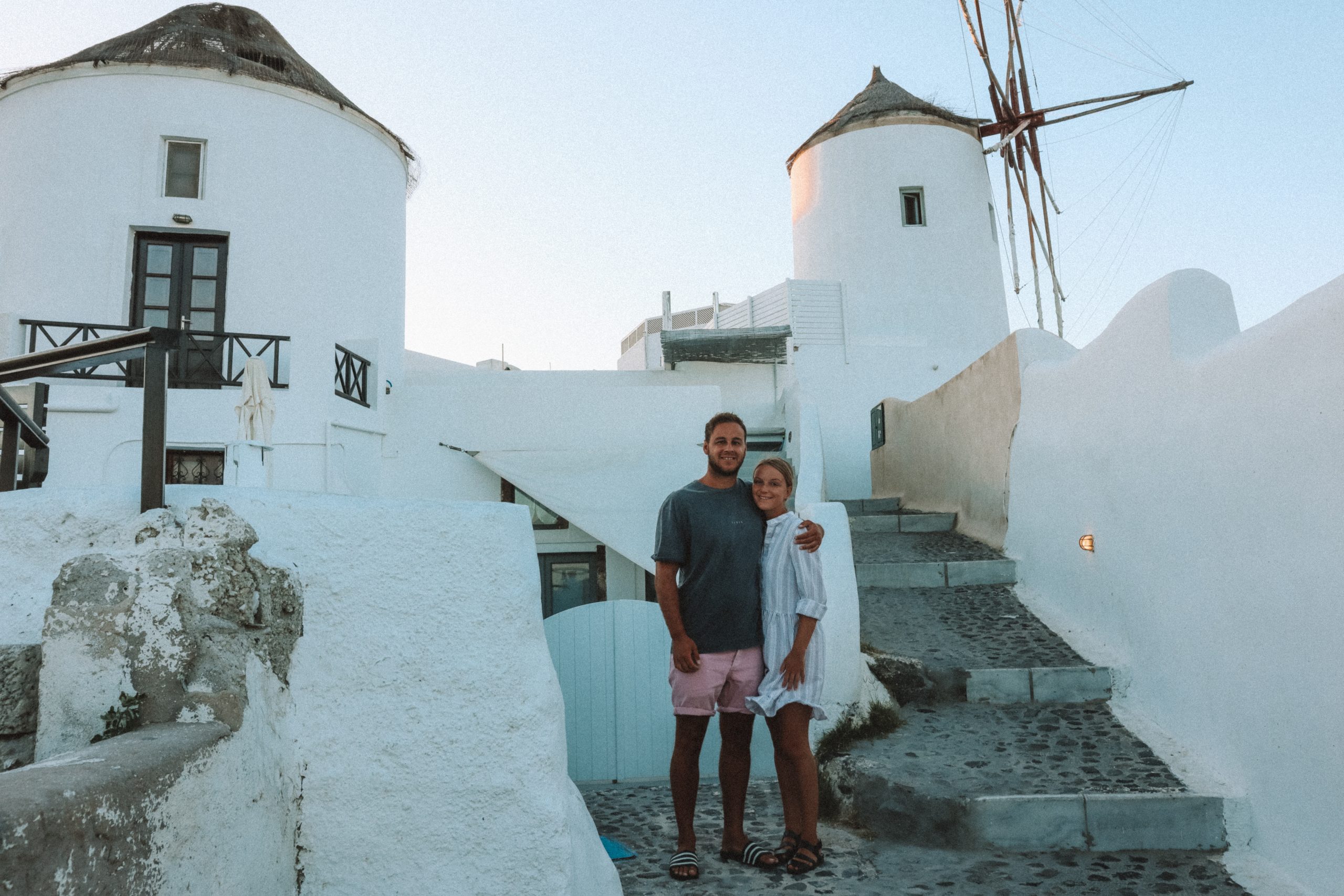 A couple stood in front of two windmills in Santorini