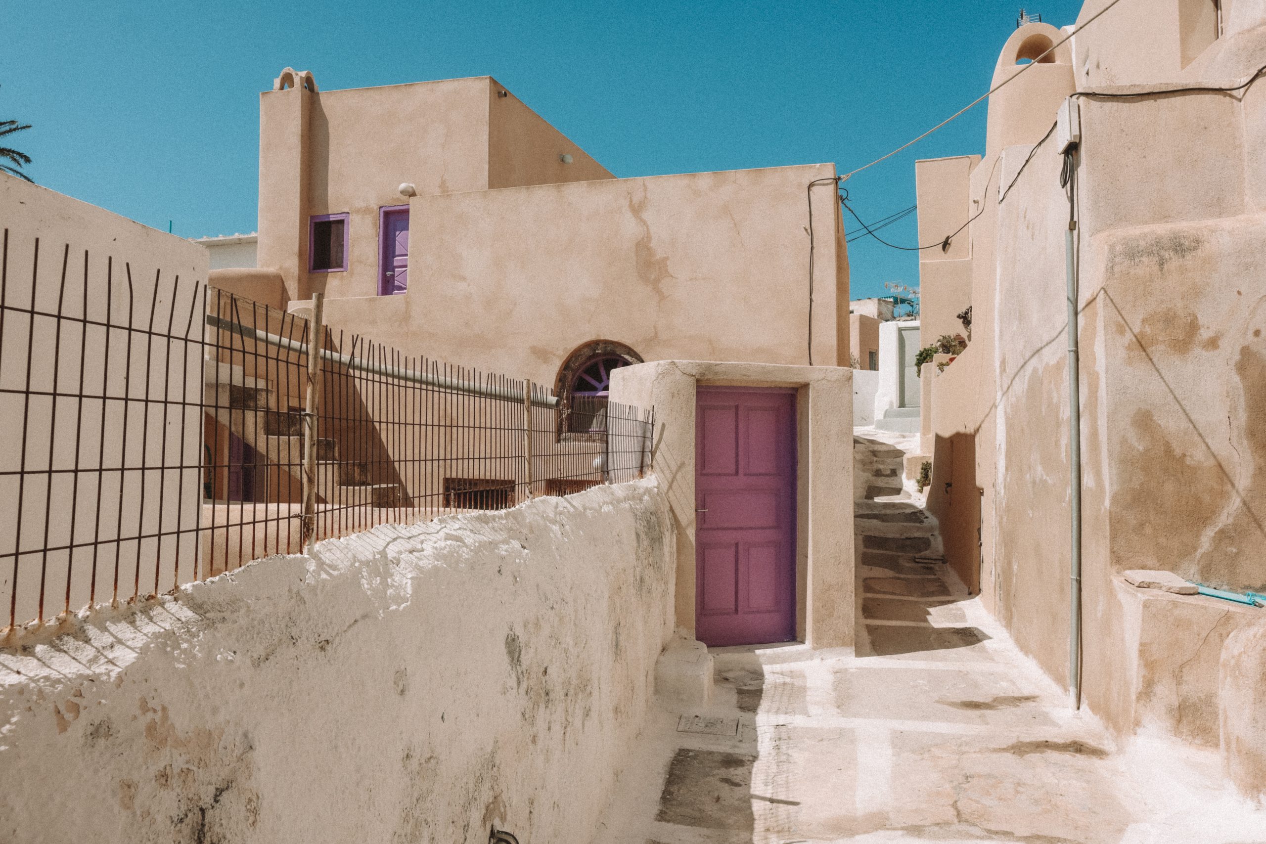 Village alleyway in Emporio with peach washed houses and purple doors. Things to do in Santorini