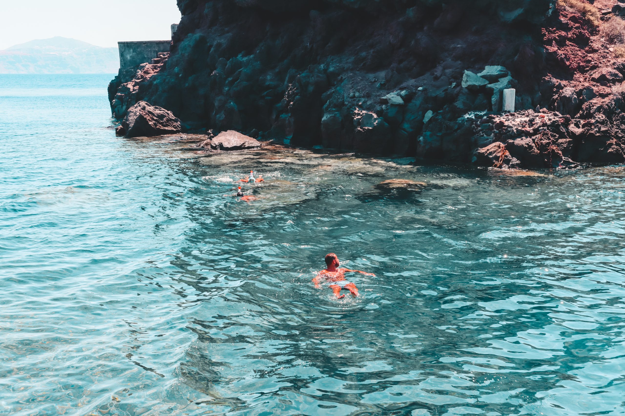 A man swimming in turquoise waters around the rocks of Ammoudi Bay
