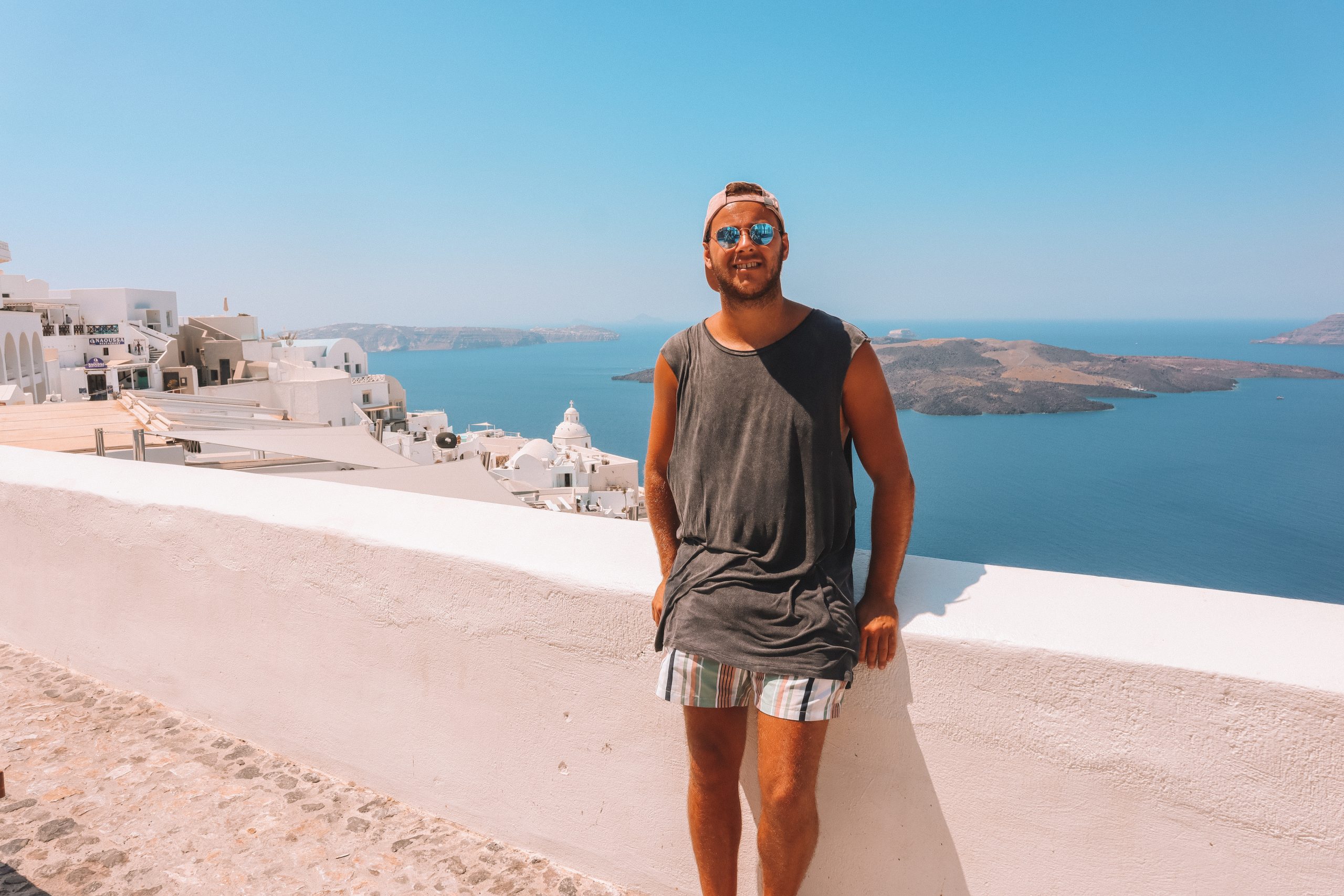 A man sat on a wall with islands in the background of Thira, Santorini