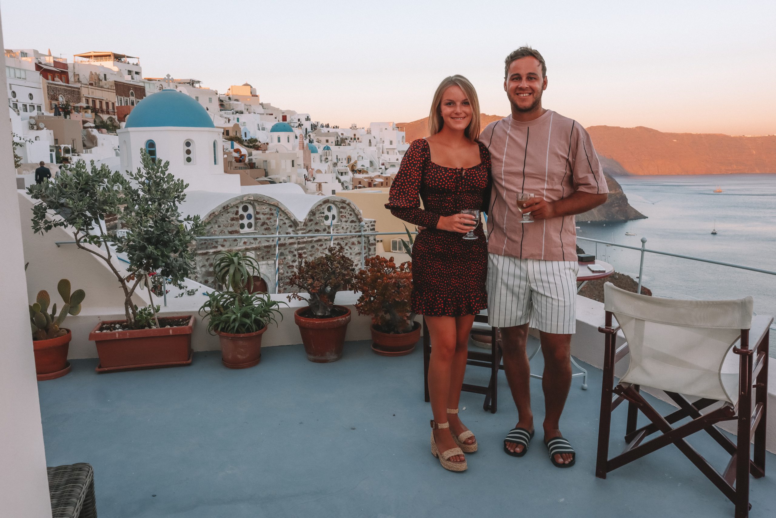 A couple stood on their balcony with blue domed churches and ocean in the background in Santorini
