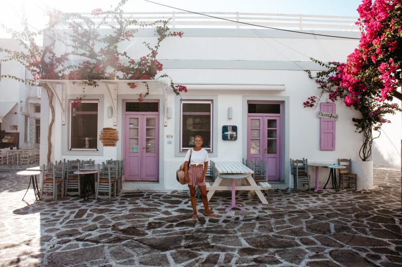 A woman stood in front of a pink and white colourful building in Antiparos.