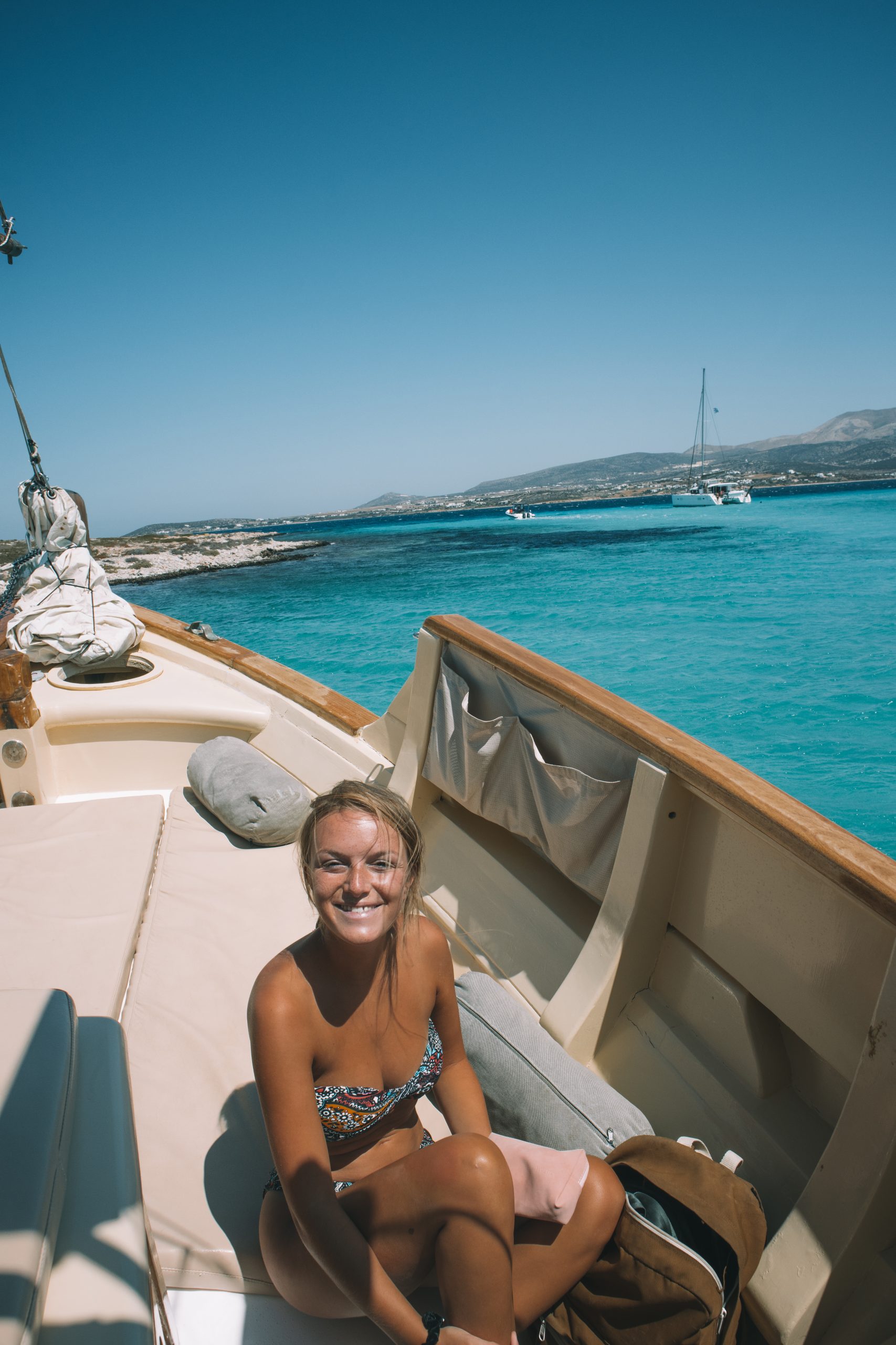 A woman smiling sat on a boat with the turquoise ocean in the background. Antiparos travel blog