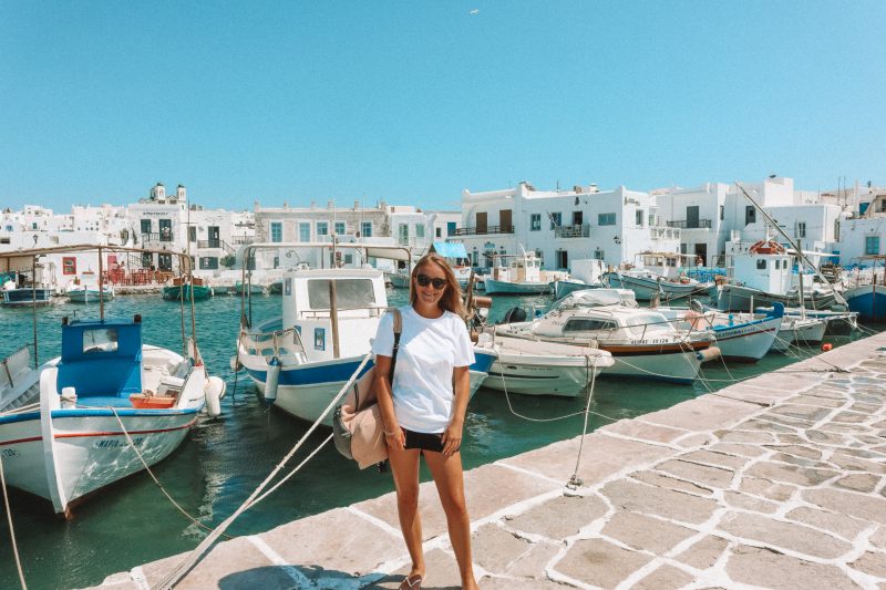 A woman stood infront of boats and whitewashed houses in Naoussa, Paros.