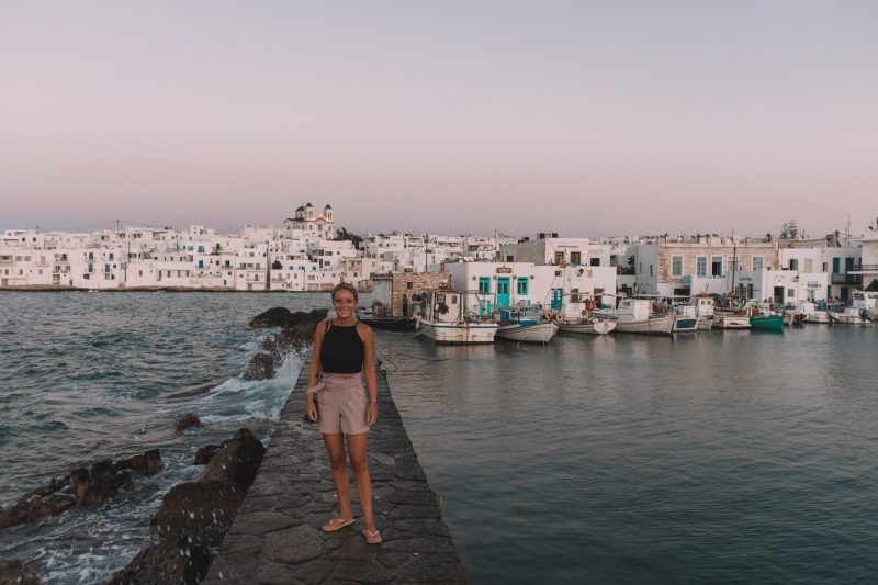 A woman stood on a sea breaker next to a harbour. Things to do in Paros