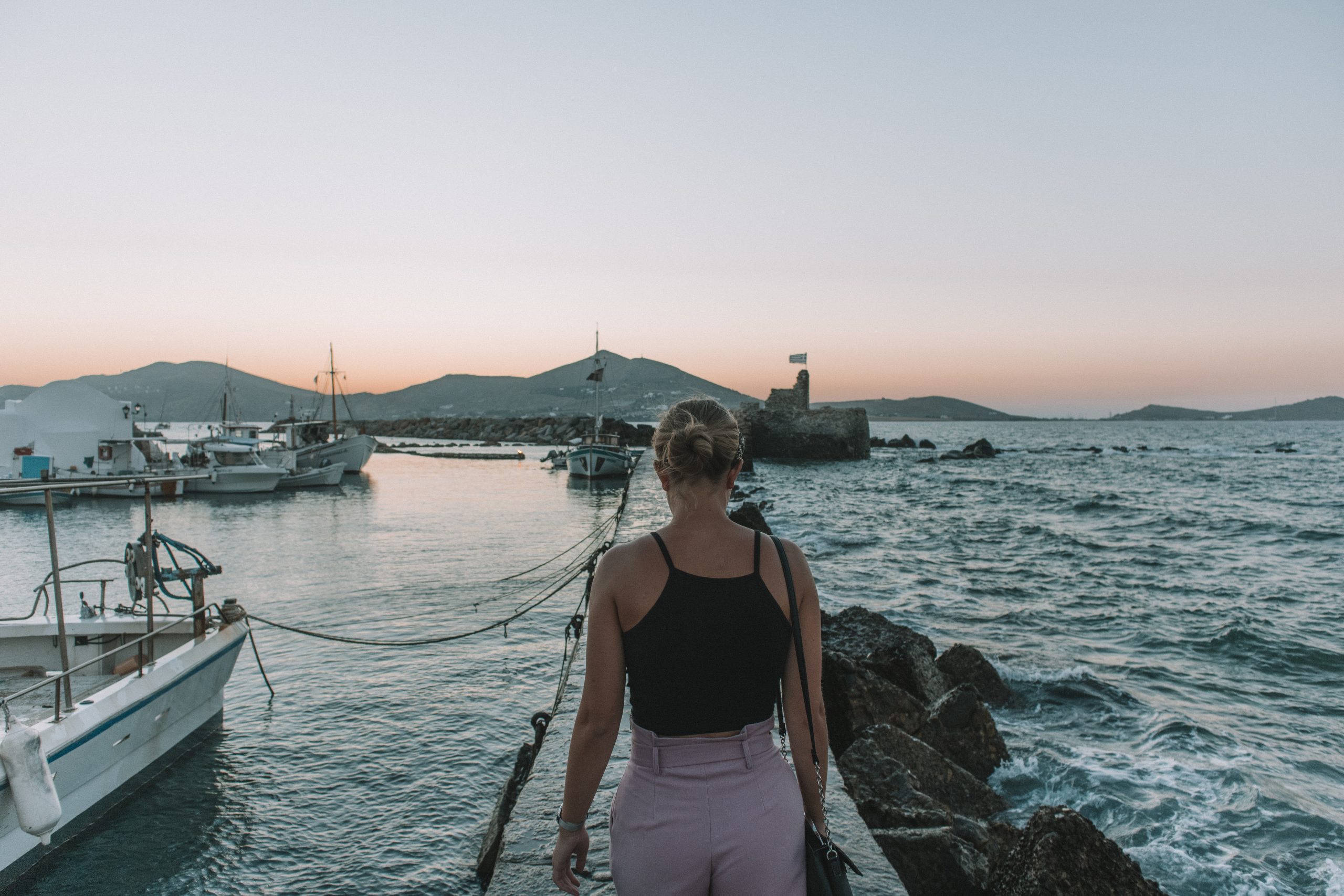 A woman walking on a sea-soaked path at sunset. Paros travel blog.