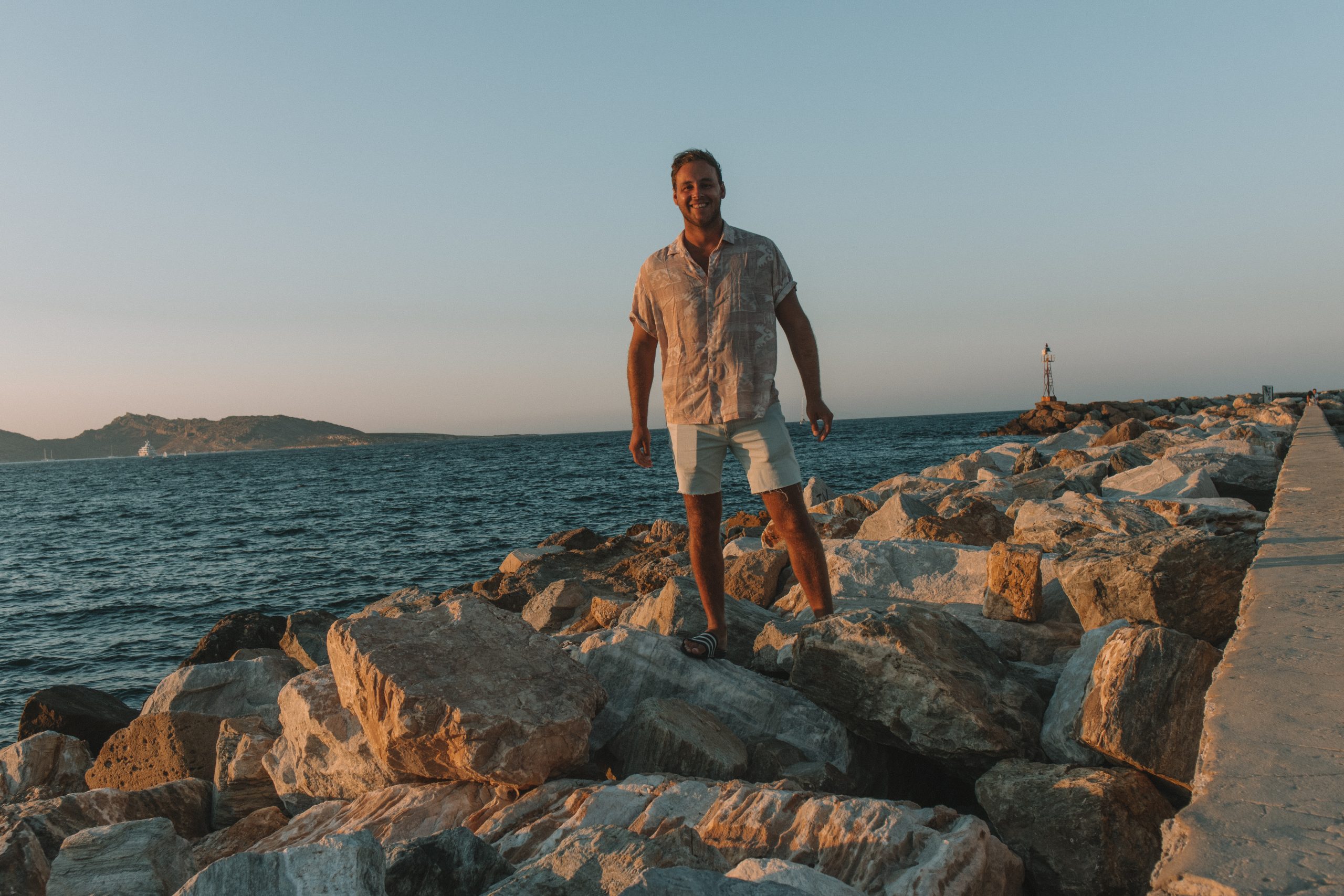 A man stood on the rocks during sunset at Naoussa harbour. Things to see in Paros